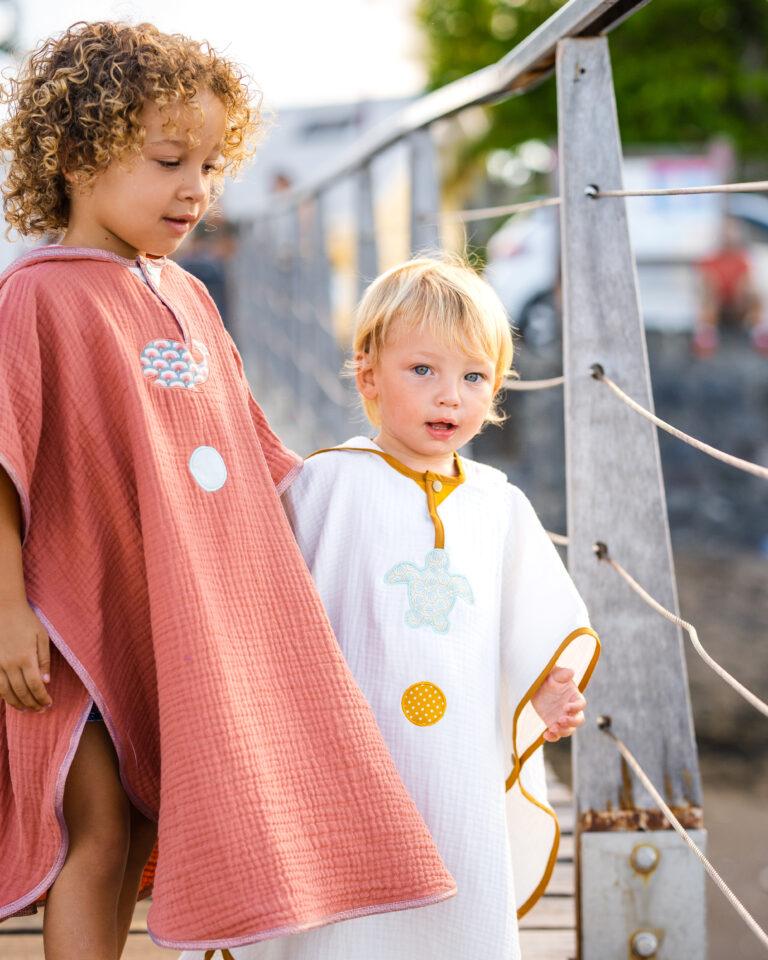 Deux enfants dans des ponchos de bain artisanales se tenant sur un trottoir au crépuscule.