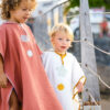 Deux enfants dans des ponchos de bain artisanales se tenant sur un trottoir au crépuscule.