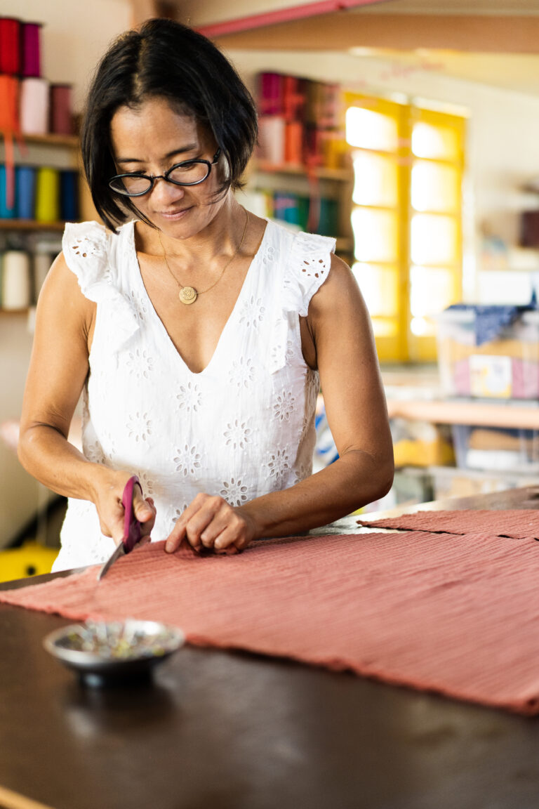 Une femme concentrée coupe du tissu sur une table de travail, illustrant l'artisanat en action.