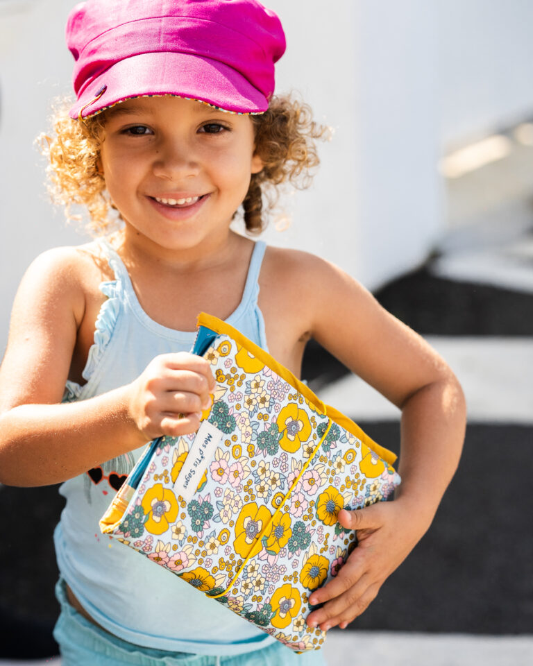 Enfant souriant tenant un carnet de croquis aux motifs floraux.