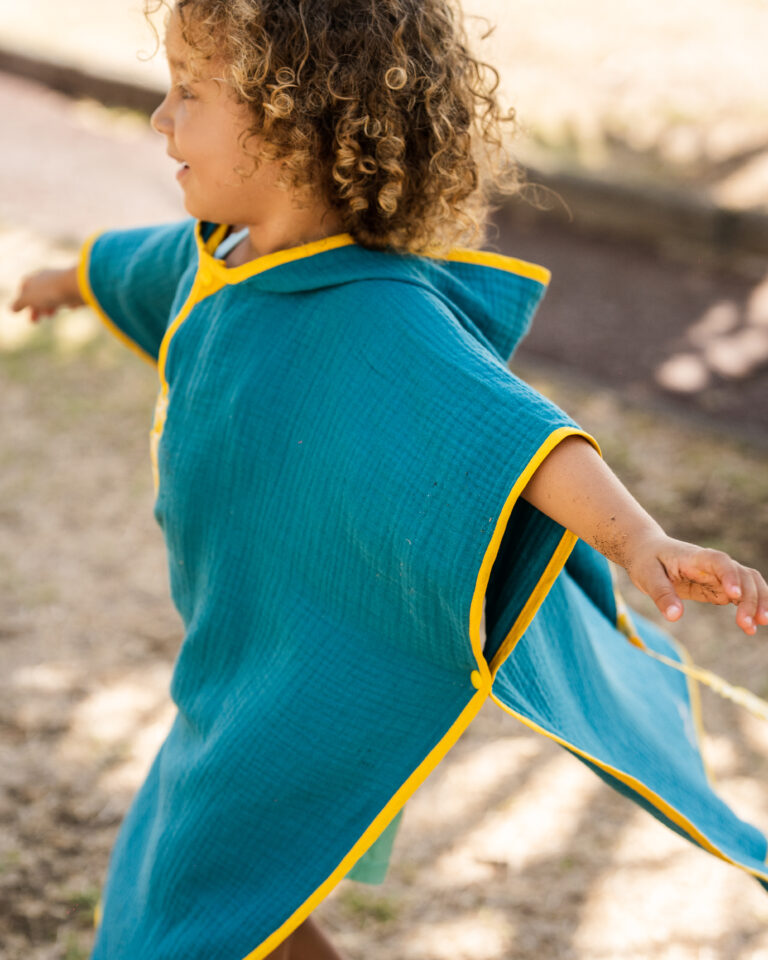 Un enfant en mouvement, son poncho de bain artisanale bleue s'écartant dans l'air.