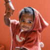 Un enfant souriant tenant la main de quelqu'un hors de l'image, vêtu d'un poncho de bain rouge avec un motif de baleine brodé.
