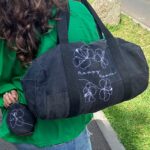 Sac de sport en denim noir avec broderie blanche de fleurs et l'inscription 'happy human'.