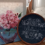 Décoration murale artisanale avec peinture de fleurs roses et broderie 'Welcome' sur fond en jean.