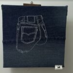 Œuvre d'art textile représentant une broderie blanche de poche de jean sur fond en denim.